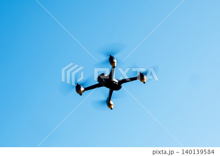 Black drone fllying in the blue sky. Innovative modern technology for work, game or entertainment. Black drone fllying in the blue sky. Innovative modern technology for work, game or entertainment. 140139584