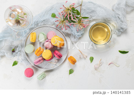 Colorful french macaroon cakes. Macaroons with jasmine flowers and tea on white table background. Selective focus 140141385