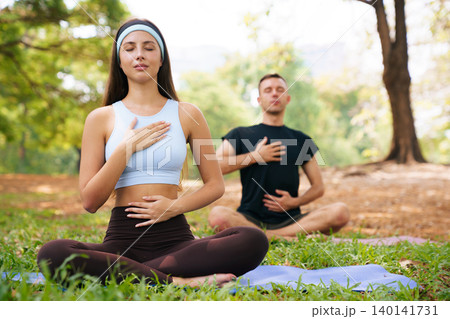 Young woman and man practicing breathing exercise in green park Young woman and man practicing breathing exercise in green park 140141731