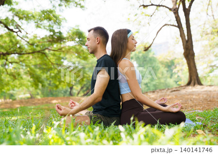 Peaceful man and woman practicing yoga meditation under large tree in park 140141746