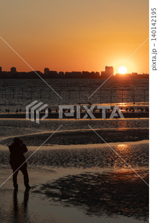 夕日の干潟でシャッターを切るカメラマンのシルエット 夕日の干潟でシャッターを切るカメラマンのシルエット 140142195