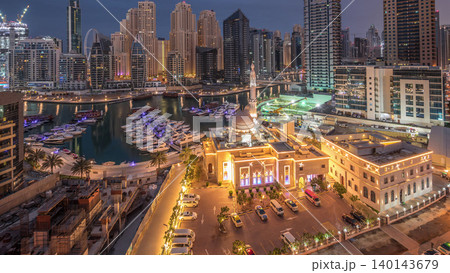 Yachts in Dubai Marina flanked by the Al Rahim Mosque and residential towers and skyscrapers aerial night to day timelapse. 140143679