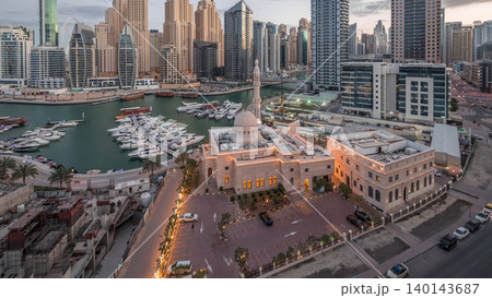 Yachts in Dubai Marina flanked by the Al Rahim Mosque and residential towers and skyscrapers aerial night to day timelapse. 140143687