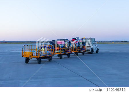 Tow tractor pulling luggage carts at evening airport 140146213