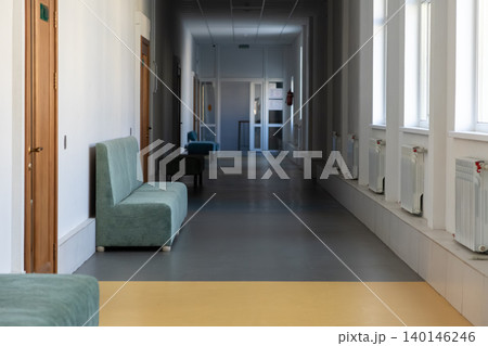 Empty office hallway with minimalist teal sofas and white walls, creating a clean professional environment for a modern business waiting room or a quiet school educational institution Empty office hallway with minimalist teal sofas and white walls, creating a clean professional environment for a modern business waiting room or a quiet school educational institution 140146246