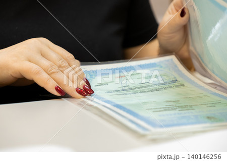 A person holds a blue certificate in a clear plastic sleeve at a white desk to represent professional verification, official documentation, success and personal achievement goals 140146256
