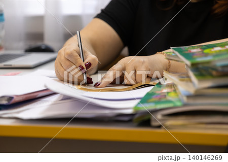 A professional person writes with a pen in a notebook at a cluttered office desk, representing productive academic research, administrative tasks, and diligent work management A professional person writes with a pen in a notebook at a cluttered office desk, representing productive academic research, administrative tasks, and diligent work management 140146269