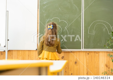 A young girl draws a bright flower with white chalk on a green classroom board to illustrate academic creativity and childhood learning moments in a sunny school environment A young girl draws a bright flower with white chalk on a green classroom board to illustrate academic creativity and childhood learning moments in a sunny school environment 140146314