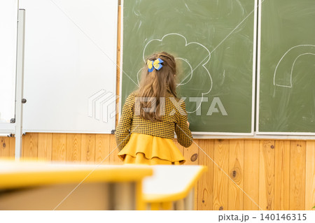 A young student draws a vibrant flower with white chalk on a classroom blackboard to demonstrate creative learning, artistic expression, and childhood education in a school setting A young student draws a vibrant flower with white chalk on a classroom blackboard to demonstrate creative learning, artistic expression, and childhood education in a school setting 140146315