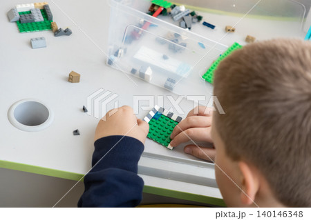 A young child is focused on assembling a complex model using colorful plastic building blocks at a desk, showcasing creativity and learning during indoor play in a bright home A young child is focused on assembling a complex model using colorful plastic building blocks at a desk, showcasing creativity and learning during indoor play in a bright home 140146348