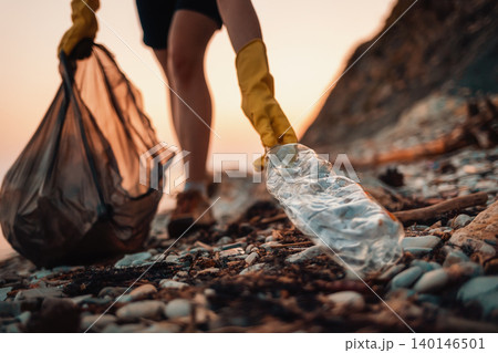 Close up of volunteer's hands with plastic bag picks up a dirty bottle. The concept of Earth Day and envinmental pollution Close up of volunteer's hands with plastic bag picks up a dirty bottle. The concept of Earth Day and envinmental pollution 140146501