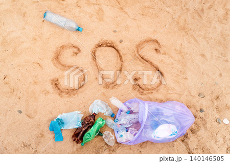 Trash bag with plastic bottles on a sandy beach. Text SOS on a sand. Top view. The concept of environmental protection and conservation Trash bag with plastic bottles on a sandy beach. Text SOS on a sand. Top view. The concept of environmental protection and conservation 140146505