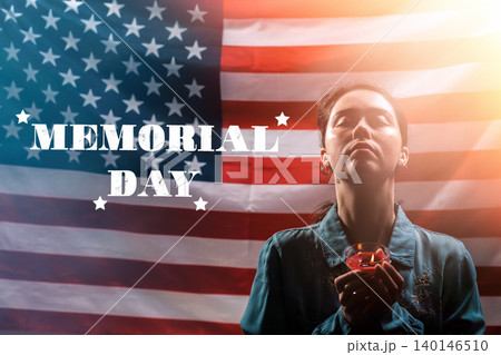Memorial day inscription. A woman holds a candle in memory of the victims and raised her head with her eyes closed. The American flag is in the background. Concept of American holidays 140146510