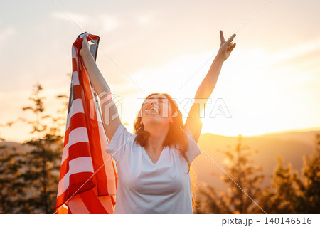 Victory. Happy patriotic young woman has risen an American flag in her hands. Sunset in the background. The concept of American Independence day Victory. Happy patriotic young woman has risen an American flag in her hands. Sunset in the background. The concept of American Independence day 140146516