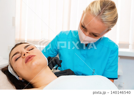 Plastic surgery at cosmetology salon. Doctor in gloves and protective mask makes a syringe injects to the female client. Lifting and aesthetic medicine Plastic surgery at cosmetology salon. Doctor in gloves and protective mask makes a syringe injects to the female client. Lifting and aesthetic medicine 140146540