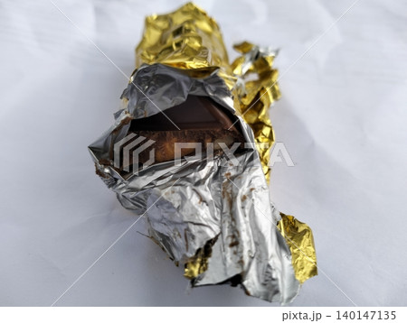 Partially Unwrapped Milk Chocolate Bar in Gold Foil Isolated on White 140147135