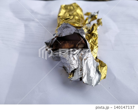 Partially Unwrapped Milk Chocolate Bar in Gold Foil Isolated on White 140147137