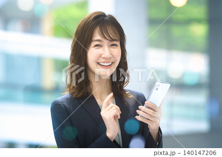 スマートフォンを手に笑顔を見せる日本人ビジネスウーマン スマートフォンを手に笑顔を見せる日本人ビジネスウーマン 140147206