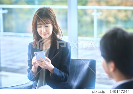 スマートフォンの画面を見せながら商談する日本人女性 スマートフォンの画面を見せながら商談する日本人女性 140147244