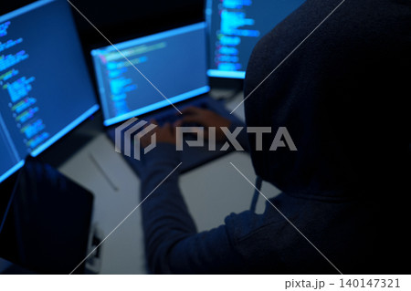 Hacker Working at Multiple Monitors in Dark Room 140147321