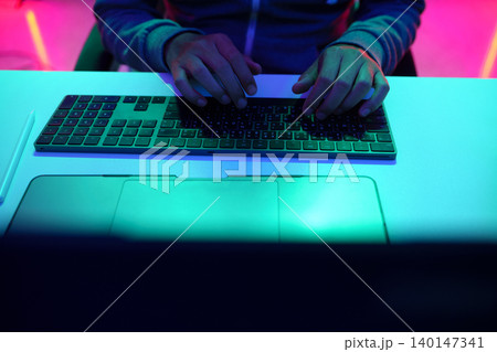 Hands Typing on Keyboard Under Neon Light 140147341