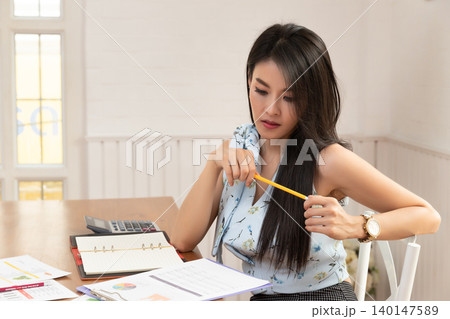 Charming young Asian woman holding a pencil while thinking when looking at the document in office. 140147589