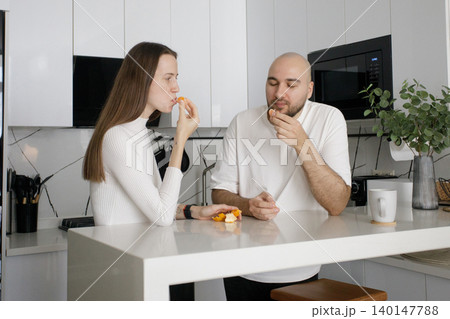 Attractive couple eating fruit and drinking coffee in domestic kitchen at home 140147788