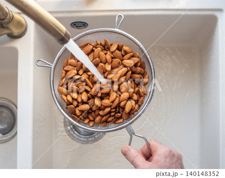 Man washes almonds in a metal colander 140148352