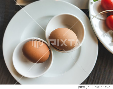Two brown eggs in white cups on a plate Two brown eggs in white cups on a plate 140148392