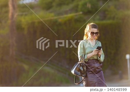 Cheerful Woman Browsing Smartphone Outdoors at Golden Hour Cheerful Woman Browsing Smartphone Outdoors at Golden Hour 140148599