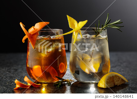 A gin and tonic and an Old Fashioned in frosted glasses on a black table. A gin and tonic and an Old Fashioned in frosted glasses on a black table. 140148641