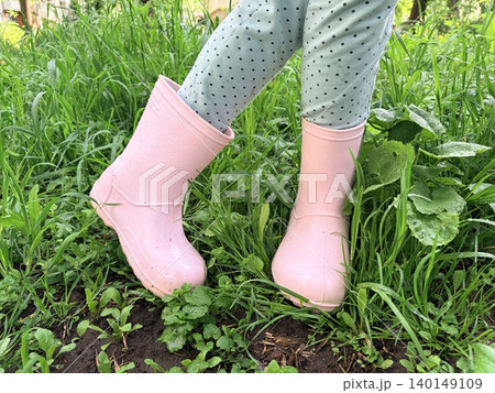 a girl's lower legs standing in a lush, grassy area. They are wearing light blue leggings with small black polka dots and a pair of soft pink rubber rain boots. a girl's lower legs standing in a lush, grassy area. They are wearing light blue leggings with small black polka dots and a pair of soft pink rubber rain boots. 140149109