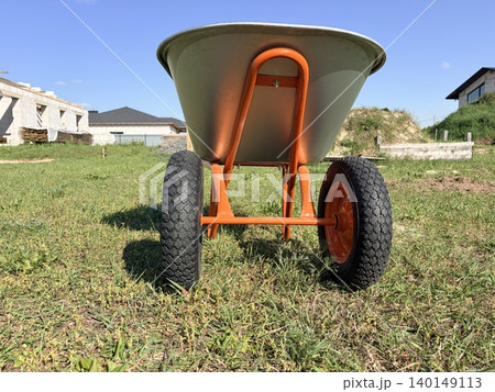 a sturdy, two-wheeled wheelbarrow positioned centrally on a patch of green grass 140149113