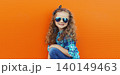 Happy cheerful kid girl with curly hair, joyful little child having fun in the city on orange wall 140149463