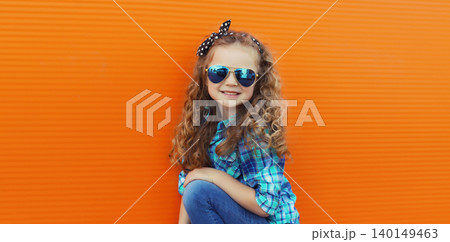 Happy cheerful kid girl with curly hair, joyful little child having fun in the city on orange wall 140149463