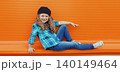 Happy cheerful kid girl dancer with curly hair, joyful child dancing in the city on orange wall 140149464