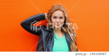 Portrait beautiful young blonde woman posing in black leather jacket on colorful orange background Portrait beautiful young blonde woman posing in black leather jacket on colorful orange background 140149467
