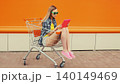 Modern young woman using digital tablet computer sitting in shopping trolley cart on city street 140149469