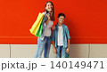 Happy smiling mother and son child together with shopping bags in city on red wall background 140149471