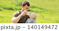 Father feeds baby from bottle sitting on grass in sunny summer park 140149472