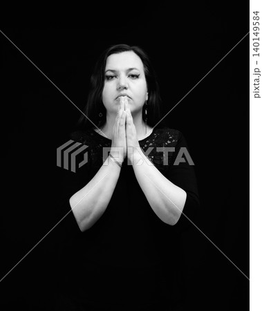 woman folded her palms together near her face in a prayer or greeting gesture on a dark background 140149584