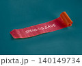 A vibrant roll of ribbon displays the phrase spend vs save on a teal background, inviting reflection on financial decisions and economic habits in daily life 140149734