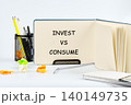A neat workspace showcases an open notebook with the words Invest vs Consume written prominently. Bright colored paper scraps add a touch of creativity to the setting 140149735