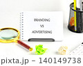 A notepad displays the words branding vs advertising while a magnifying glass and crumpled paper add a touch of creativity to the work desk 140149738