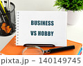 A notebook displays the words business vs hobby, creating a thoughtful atmosphere for anyone contemplating creative pursuits. Tools for productivity lay nearby, inspiring focus 140149745