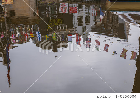 Artistic reflection of Amsterdam city architecture and international flags on canal water surface creating an abstract urban travel background in the Netherlands. Artistic reflection of Amsterdam city architecture and international flags on canal water surface creating an abstract urban travel background in the Netherlands. 140150684