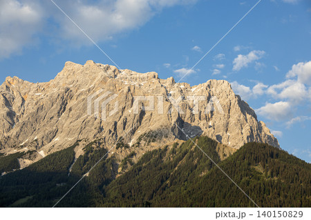 Sunlit Alpine Rock Face With Forested Slopes and Blue Sky 140150829