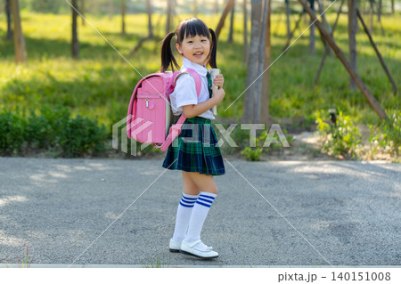 Asian primary school students walk home from school with their backpacks and books. 140151008