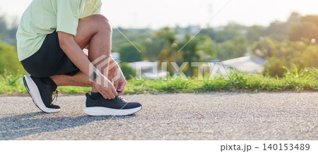 Young Asian man tying running shoes in the park. Female runner getting ready for jogging and exercise on the road. Fitness, wellness and outdoor sport concept in morning Young Asian man tying running shoes in the park. Female runner getting ready for jogging and exercise on the road. Fitness, wellness and outdoor sport concept in morning 140153489