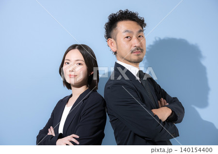 腕組みをして背中合わせのカメラ目線のスーツのビジネスマン男女 真剣で真面目な表情リーダーシップや信頼 腕組みをして背中合わせのカメラ目線のスーツのビジネスマン男女 真剣で真面目な表情リーダーシップや信頼 140154400
